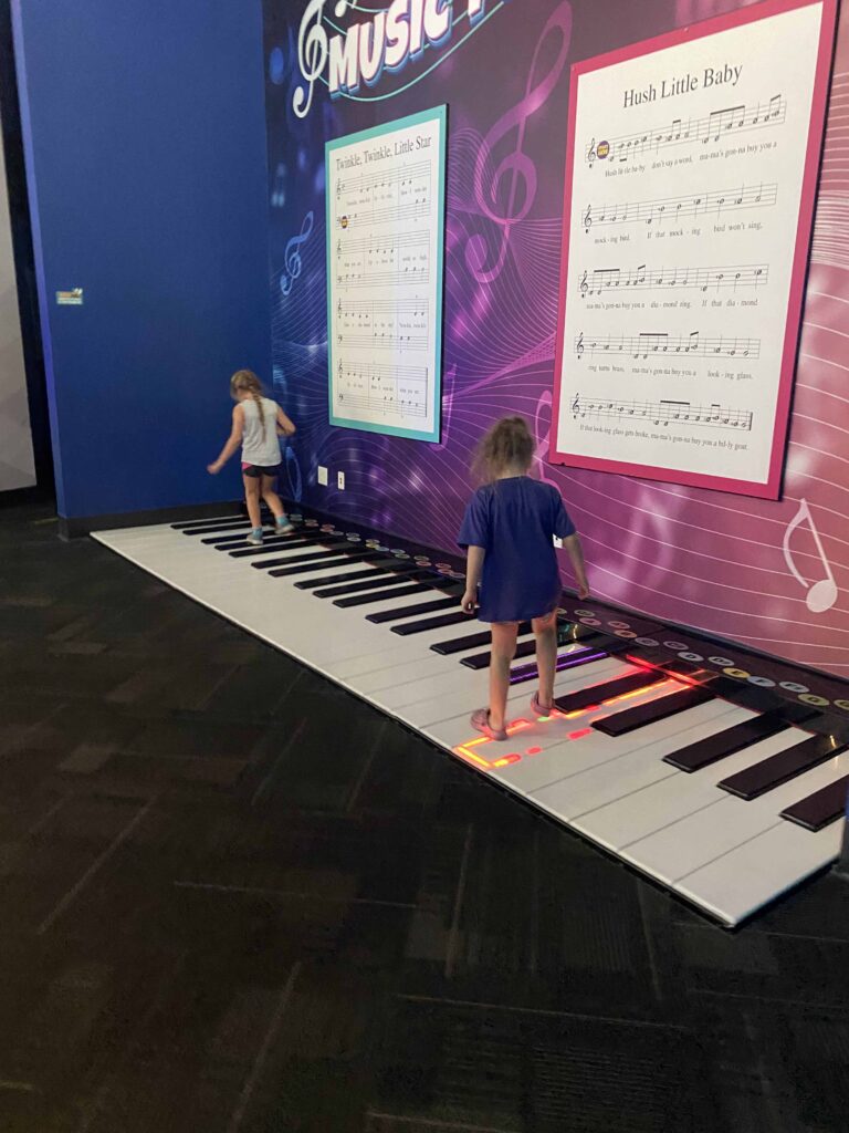 Young students play an extra large piano by standing on each of the large keys.